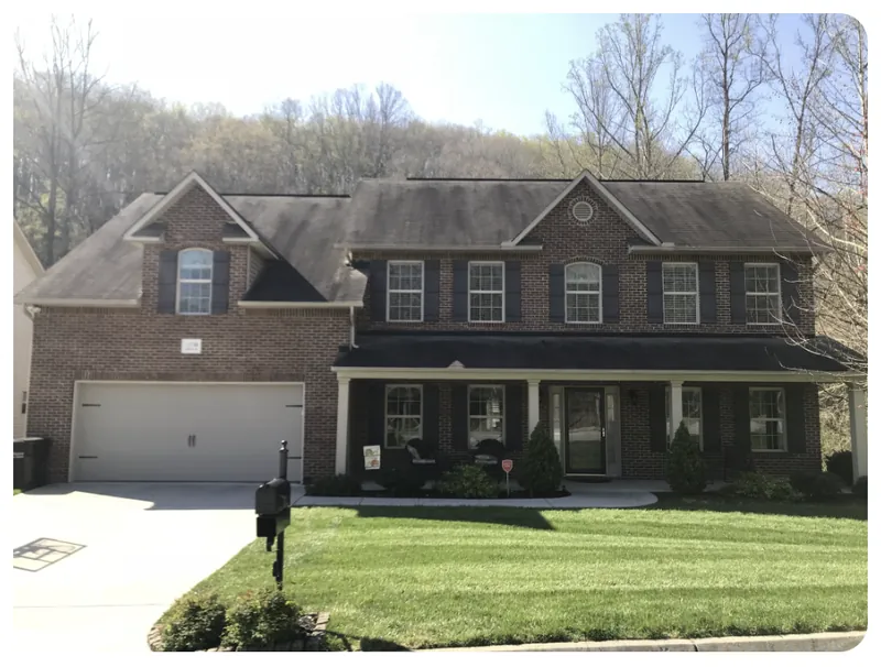 Two-story brick house roof with black mold and mildew streaks before soft wash